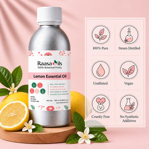 A bottle of Raasa oils Lemon Essential Oil stands on a wooden board with sliced lemons and white flowers against a soft pink background. A product information panel on the right lists benefits such as 100% Pure, Steam Distilled, Undiluted, Vegan, Cruelty Free, and No Synthetic Additives.