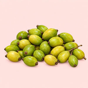 A pile of small oval green and yellow fruits with brown stems, arranged on a solid pale pink background.