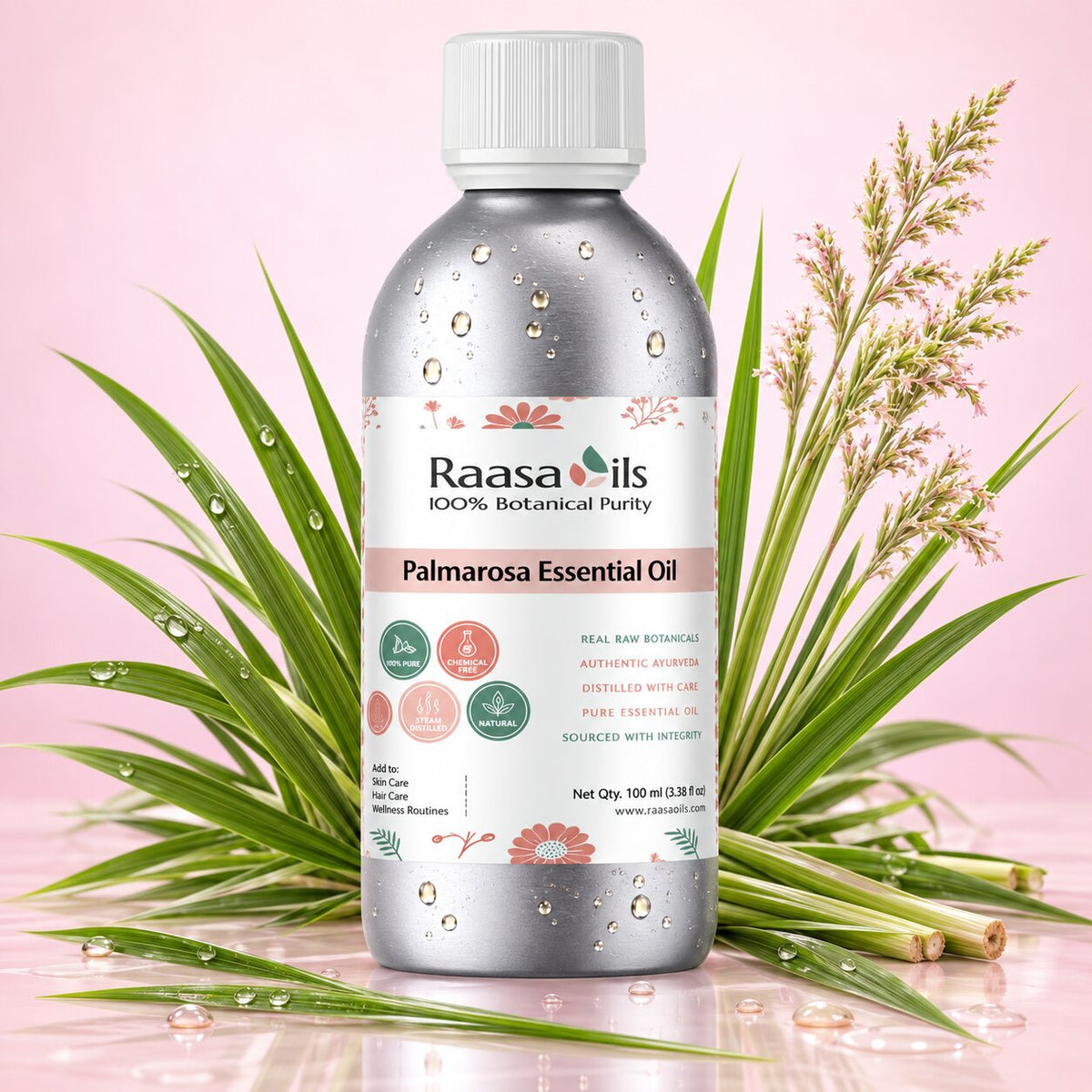 A bottle of Raasails Palmarosa Essential Oil centered on a pink background, surrounded by green leaves and dried palm fronds with water droplets. The bottle is metallic silver with a white cap and a white label featuring pink and green botanical details.