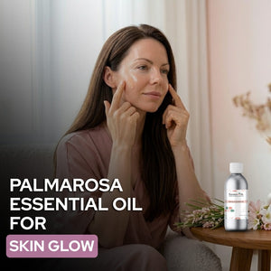Woman applying Palmarosa essential oil to her face with a bottle of the product on a table.