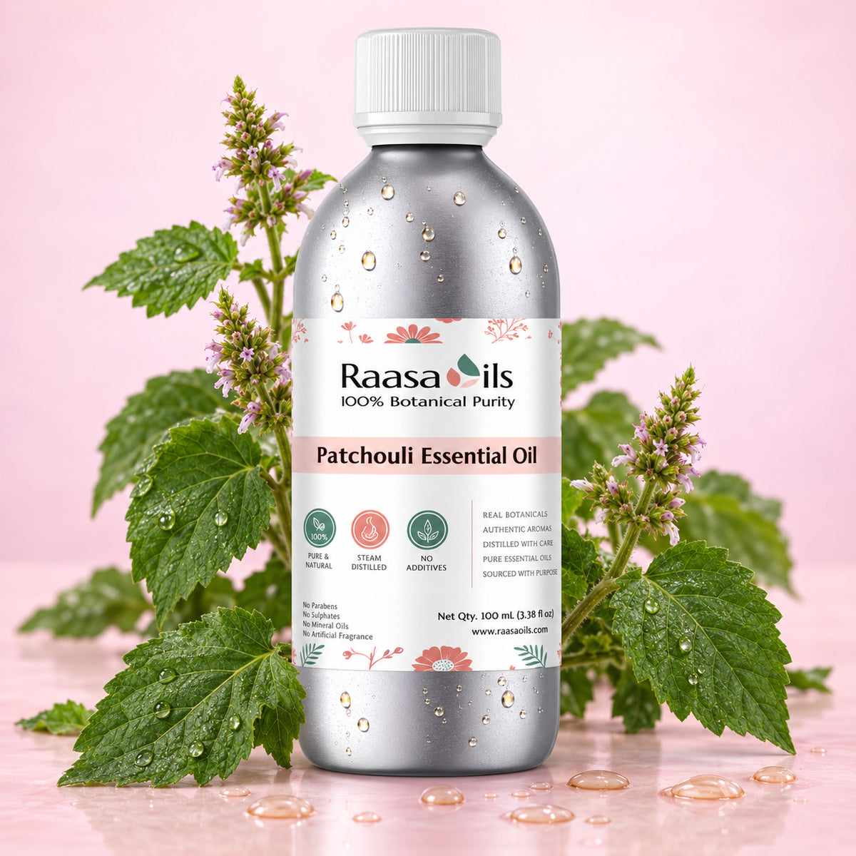 A bottle of Raasa oils Patchouli Essential Oil centered on a pink background, surrounded by fresh green patchouli leaves and small flowers. The bottle is metallic silver with a white cap and a white label featuring pink and green accents.