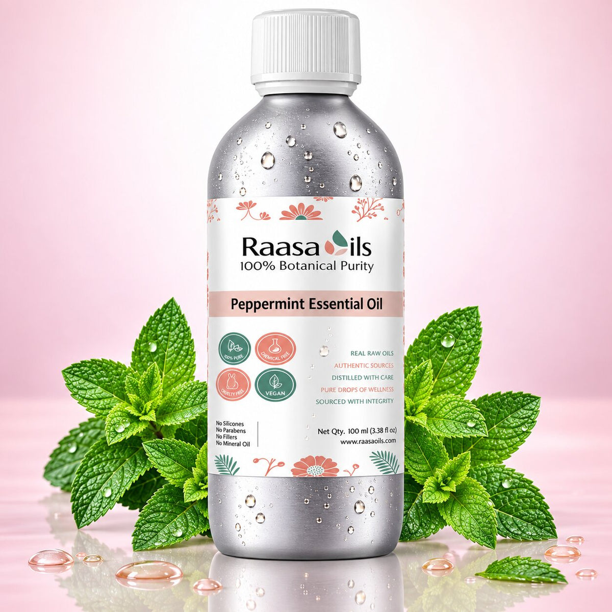 A bottle of Raasa Oils Peppermint Essential Oil centered on a soft pink background, surrounded by fresh green mint leaves and a few scattered droplets of oil. The bottle is metallic silver with a white cap and a white label featuring pink floral accents and green icons.