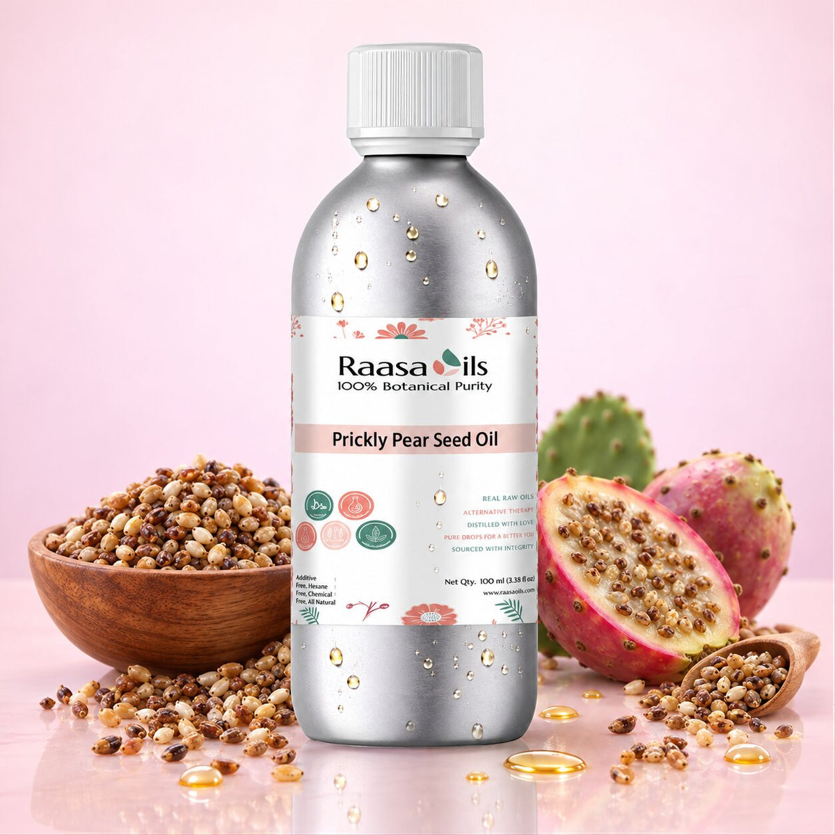 A bottle of Raasa Oils Prickly Pear Seed Oil centered on a pink background, surrounded by prickly pear fruits, a wooden bowl of seed kernels, and scattered oil droplets.