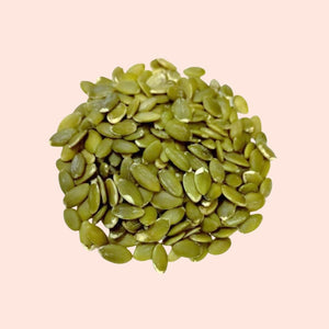 Pile of green pumpkin seeds on a light pink background