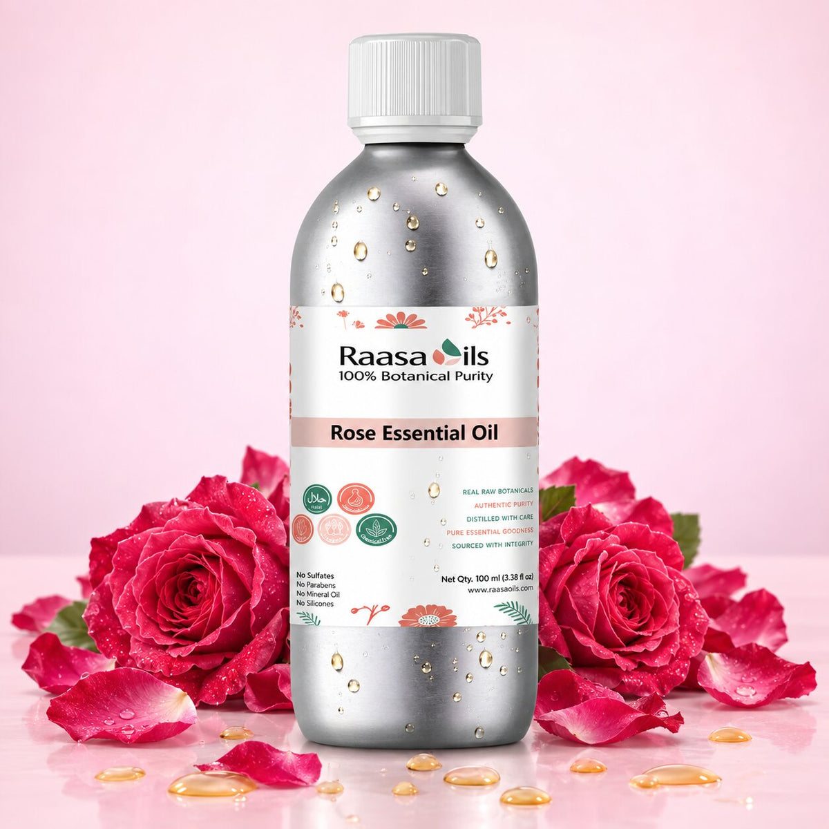 A bottle of Raasa oils Rose Essential Oil surrounded by fresh pink roses and scattered petals on a pink background.