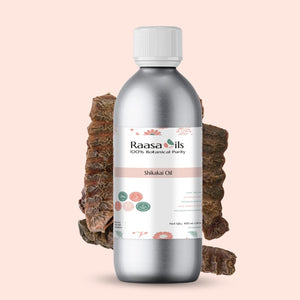 Bottle of Raasa Oils Shikakai Oil with a piece of soap root on a light pink background