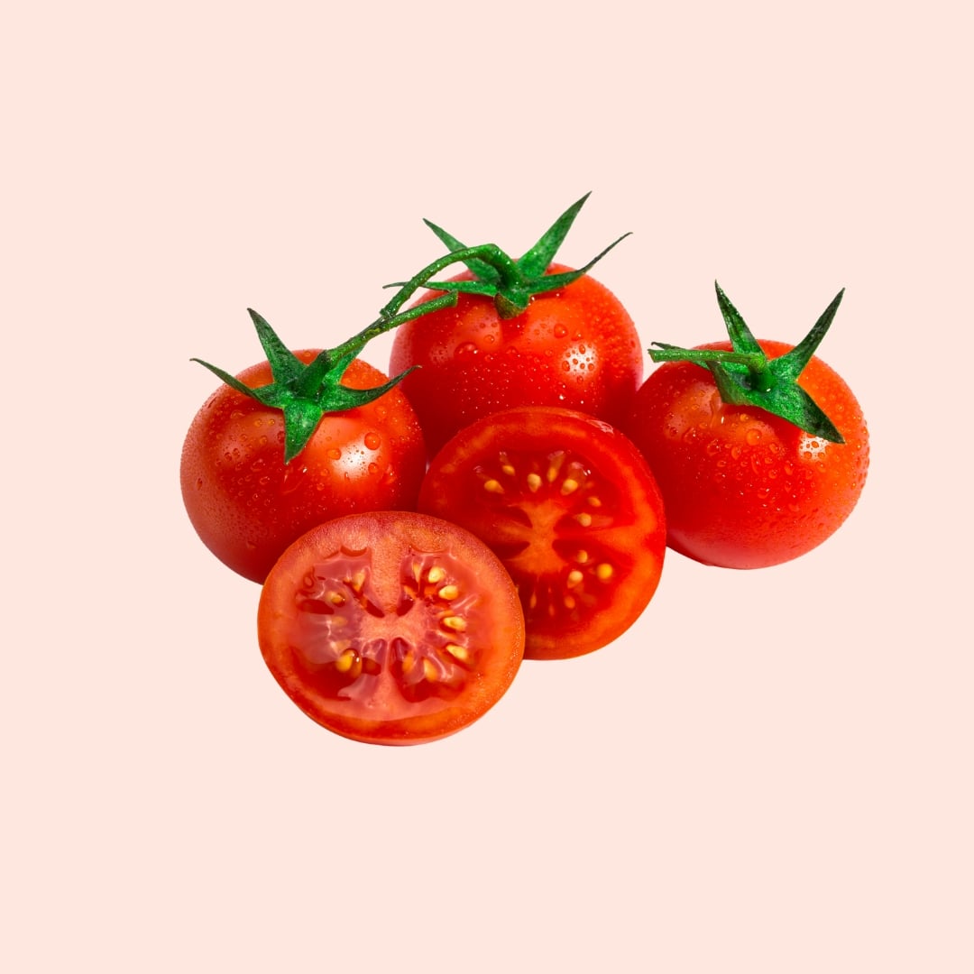 Fresh tomatoes with a cut one on a light pink background