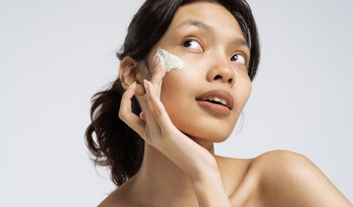 Woman applying cream to her face against a plain background